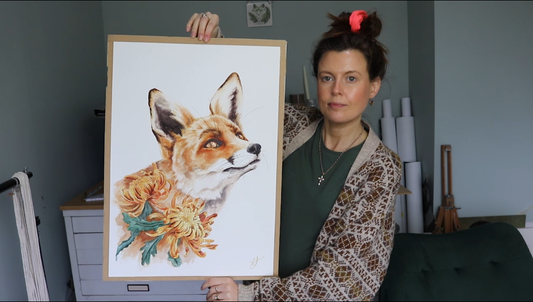 Artist holding up a watercolour painting of a fox and flowers