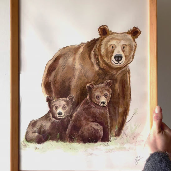 A video of the artist holding up a framed watercolour painting of three bears 